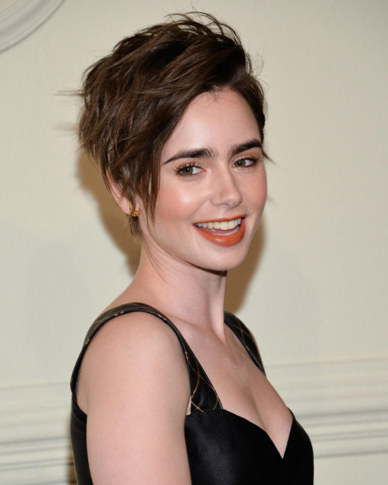 Peinados de Lily Collins para Año Nuevo; mujer de cabello lacio y castaño con corte pixie, peinado rebelde, maquillaje natural