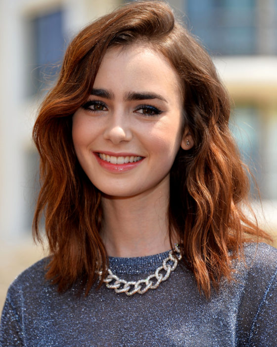 Peinados de Lily Collins para Año Nuevo; mujer de cabello castaño rojizo, ondulado, con corte long bob, maquillaje de día natural