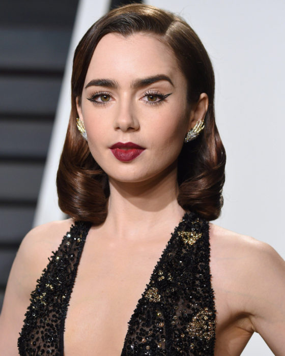 Peinados de Lily Collins para Año Nuevo; mujer de estilo retro, con peinado de los años 30, cabello corto y ondulado, maquillaje dramático y natural