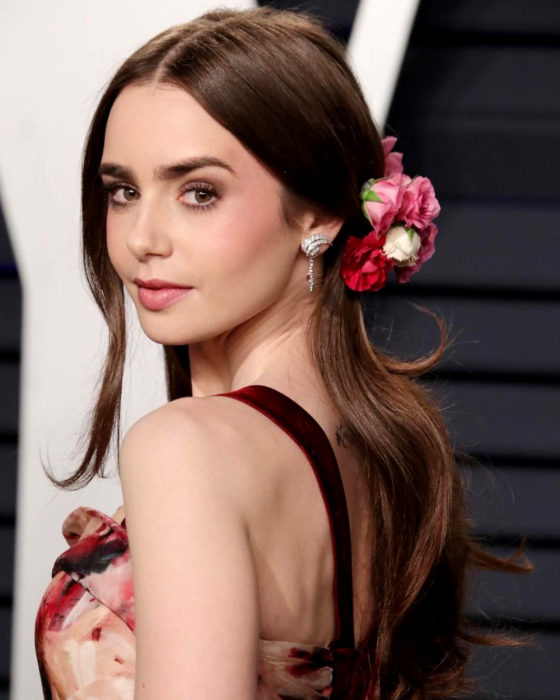 Peinados de Lily Collins para Año Nuevo; mujer de cabello largo, lacio y castaño, con tocado de flores artificiales, maquillaje natural