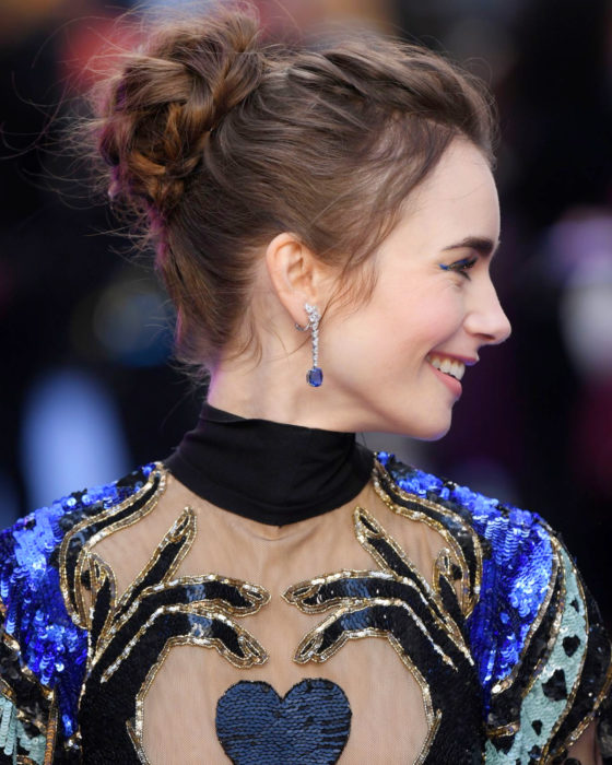 Peinados de Lily Collins para Año Nuevo; mujer de cabello largo y castaño, con peinado de chongo y trenzas romántico, vestido de lentejuelas azul con corazón negro