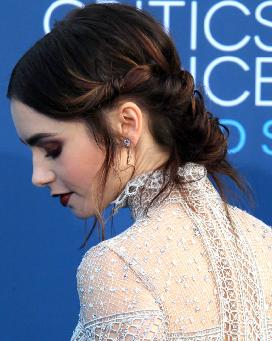 Peinados de Lily Collins para Año Nuevo; mujer de cabello castaño con luces, recogido en chongo despeinado, maquillaje color vino de noche