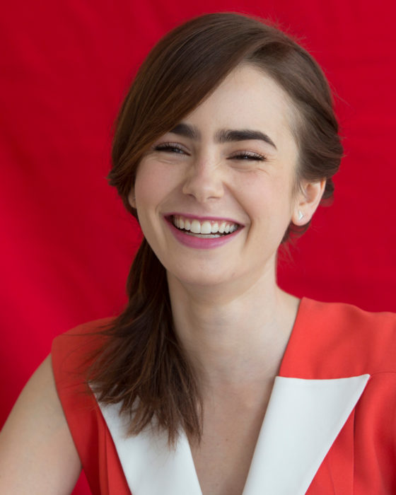 Peinados de Lily Collins para Año Nuevo; mujer de cabello lacio, mediado, castaño recogido en una coleta de lado, chica riendo