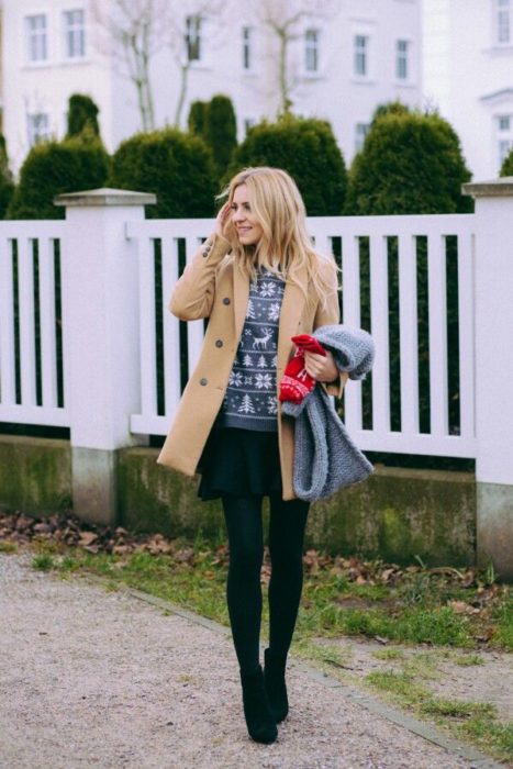 Chica usando un ugly sweter de color gris con una chaqueta café, medias, botas y falda negras 