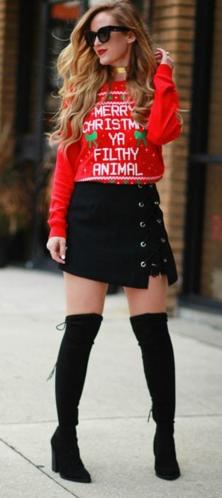 Chica usando un feo sueter navideño con botas largas y falda de color negro 