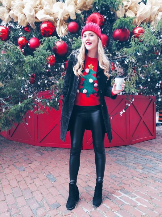 Chica usando un feo sueter navideño con una chaqueta de color negro y leggins de cuero color negros 