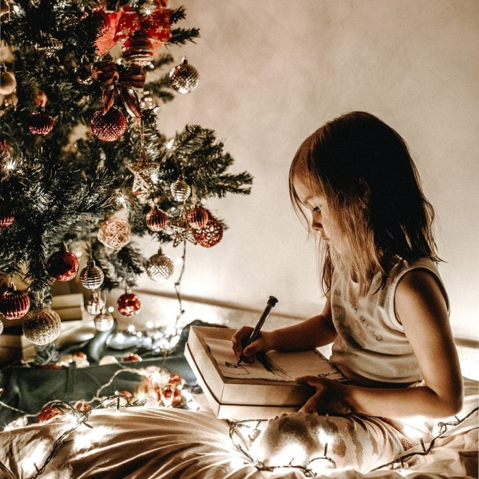 Niña escribiendo carta a Santa Claus frente al árbol de Navidad