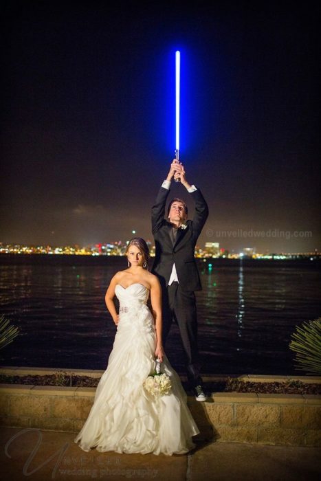 Novio sosteniendo un sable de luz mientras posa junto a su esposa en una sesión de fotos 