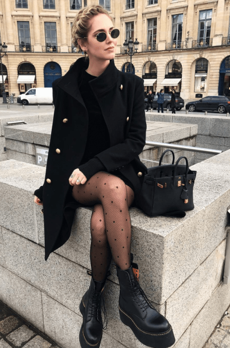 Chica sentada en una fuente mientras nuestra su outfit de coloe negro con medias estampadas 