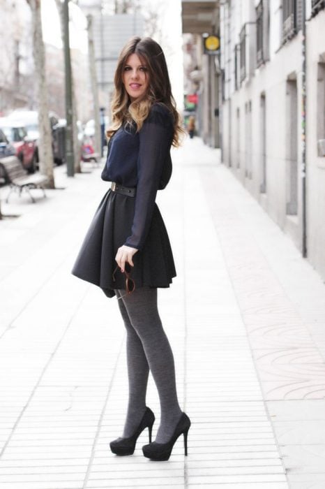 Chica usando un vestido corto de color gris con medias y tacones 
