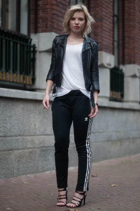 Chica usando un conjunto de pants de color negro con chaqueta de cuero y sandalias de color negro 