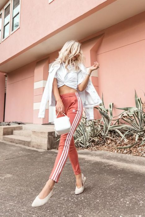 Chica posando con un outfit de pants en color coral con un abrigo y blusa de color blanco 