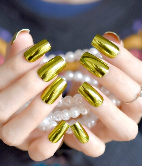 Manicure dorado para la fiesta de Año Nuevo; manos de uñas largas y cuadradas sosteniendo perlas