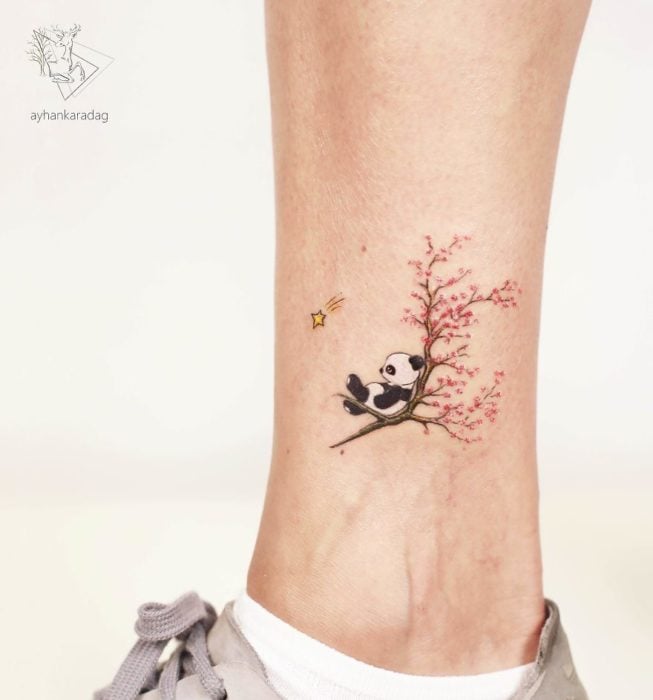 Tatuaje minimalista de un panda sentado en un cerezo 