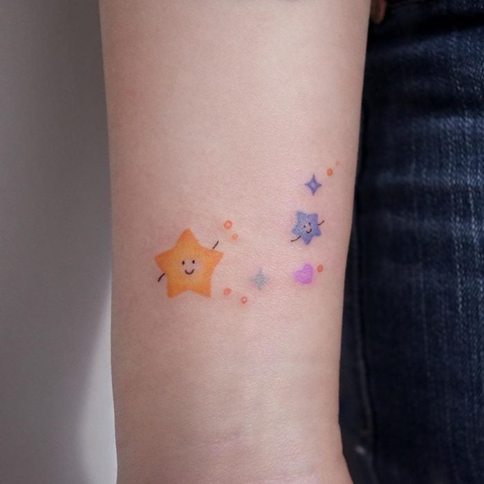Tatuaje pequeño de estrellas de colores en el brazo