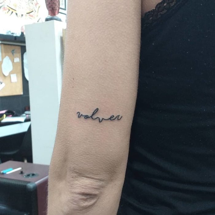 Tatuaje pequeño sobre el codo con letras volver