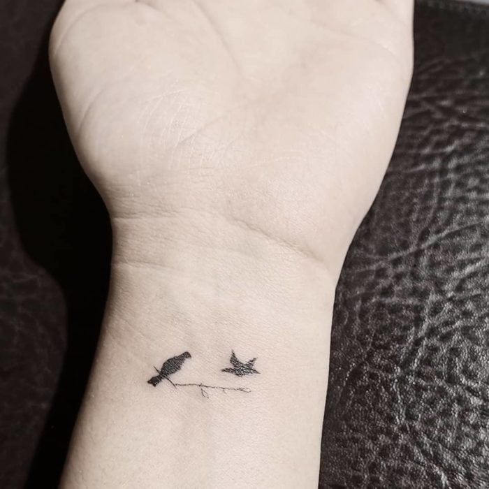 Tatuaje pequeño en la muñeca con silueta de pájaros color negro