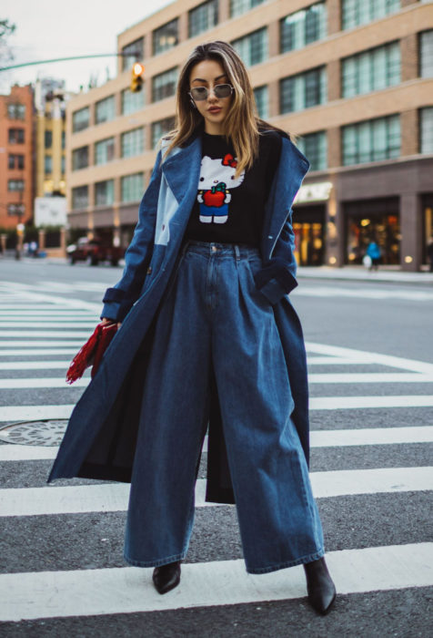 Looks con baggy jeans; mujer posando en cruce en la calle, con gabardina de mezclilla, pantalón oversized y playera de Hello Kitty