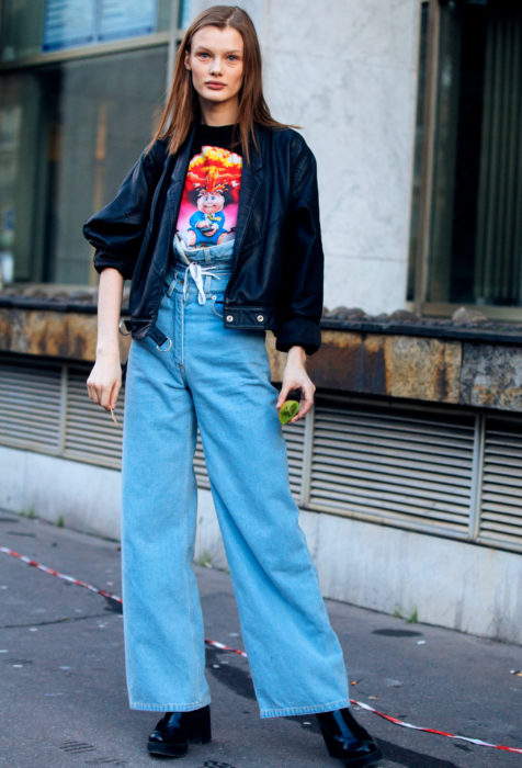 Looks con baggy jeans; mujer con chamarra de cuero negro, pantalón azul de mezclilla oversized 