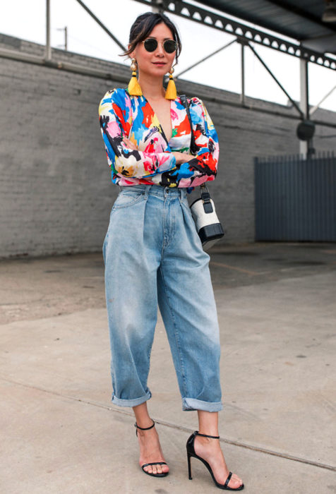 Looks con baggy jeans; mujer de lentes oscuros, aretes amarillos, blusa de colores, pantalones oversized y sandalias de tacón