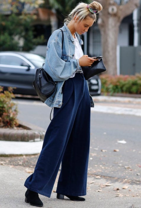 Looks con baggy jeans; mujer rubia mirando su celular en la calle con pantalones holgados y peinado de chongo alto