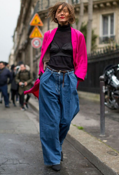 Looks con baggy jeans; mujer con look alocado, saco rosa fuscia, blusa de cuello de tortuga, pantalón oversized, chica caminando en la calle con la manos metidas en las bolsas