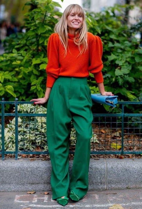Looks con baggy jeans; mujer rubia vestida con colores contrastantes y brillantes, anaranjado y verde, con pantalón holgado y suéter oversized, bolsa azul