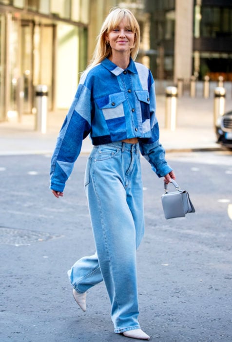 Looks con baggy jeans; mujer rubia caminando en la calle con pantalón oversized y chamarra de mezclilla, bolsa de mano mini