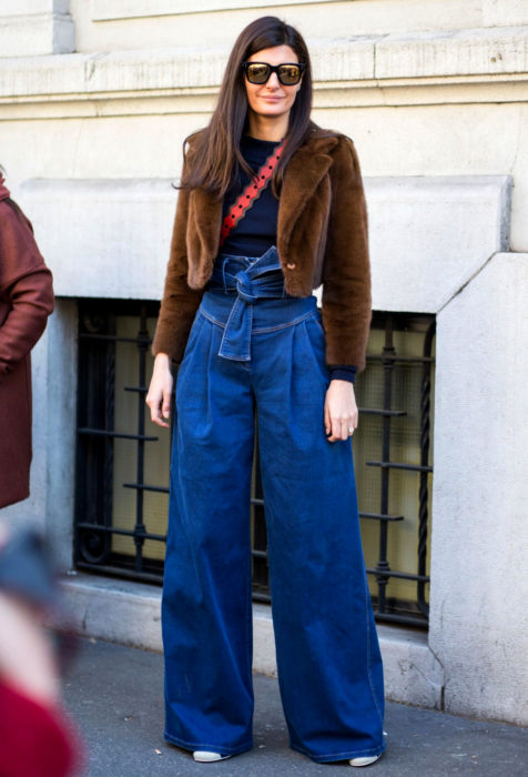 Looks con baggy jeans; mujer de cabello castaño, lacio y largo, con lentes de sol, abrigo café, pantalones oversized acampanados 