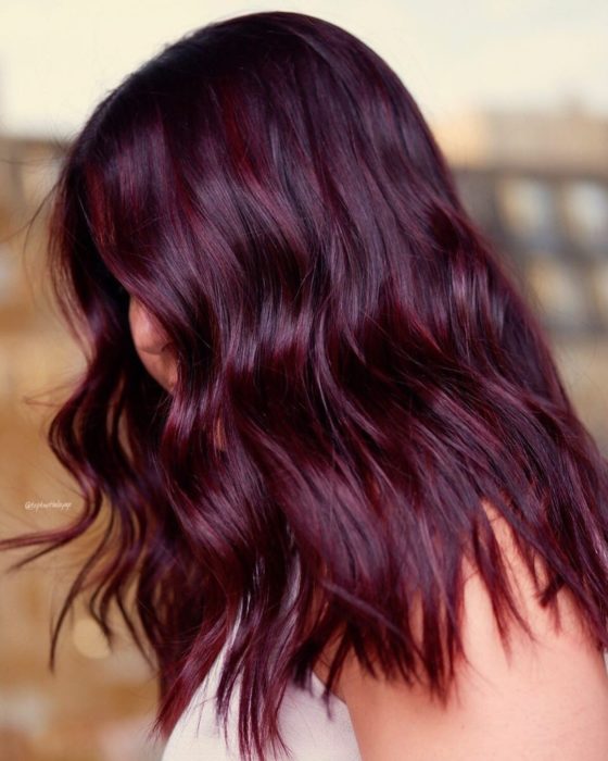 Chica de perfil mostrando su cabello con ondas en tono cherry wine y luces violeta