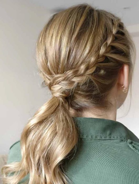 Chica rubia usando camisa verde peinada con coleta con trenza al lado y pendientes dorados