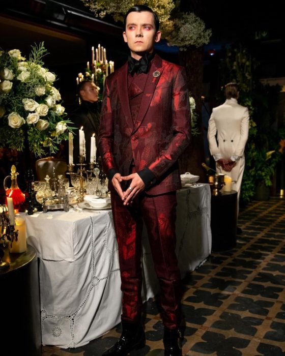 Asa Butterfield con un traje en rojo vino en un gran comedor 