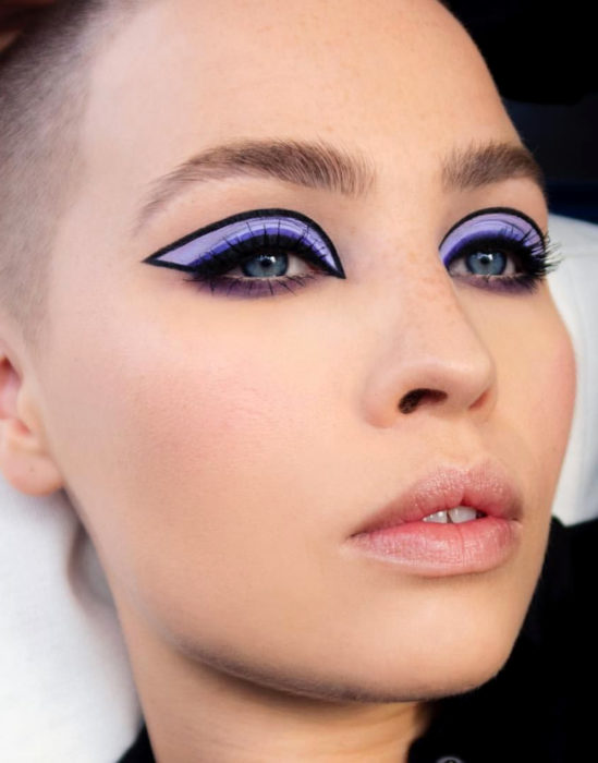 Maquillaje tendencia para el 2020;; delineado gráfico o flotante con sombra morada; mujer rapada con pecas y teeth gap