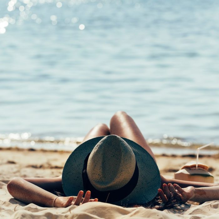 Mujer relajada en la playa, usando un sombrero para el sol y tomando agua de coco