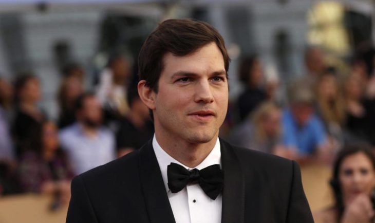 Ashton Kutcher sonriendo ligeramente para una fotografía en una alfombra roja