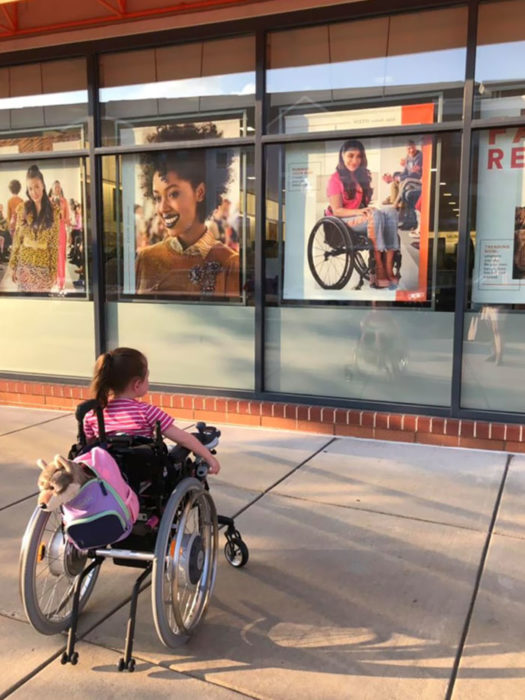 Niña en silla de ruedas viendo afiche de película con chica en silla de ruedas