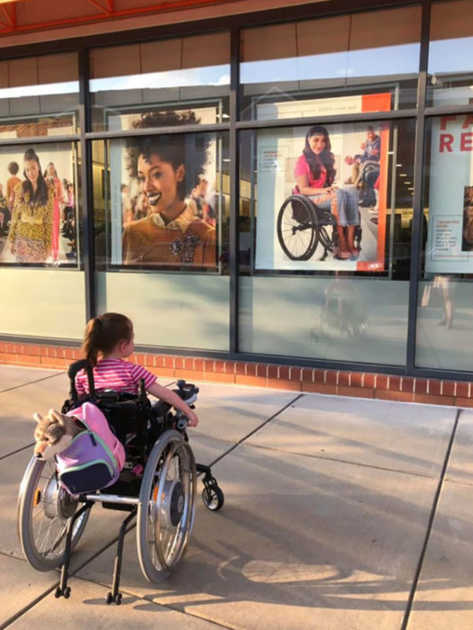 Niña en silla de ruedas viendo afiche de película con chica en silla de ruedas