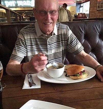 Adulto mayor comiendo sopa y hamburguesa en restaurante