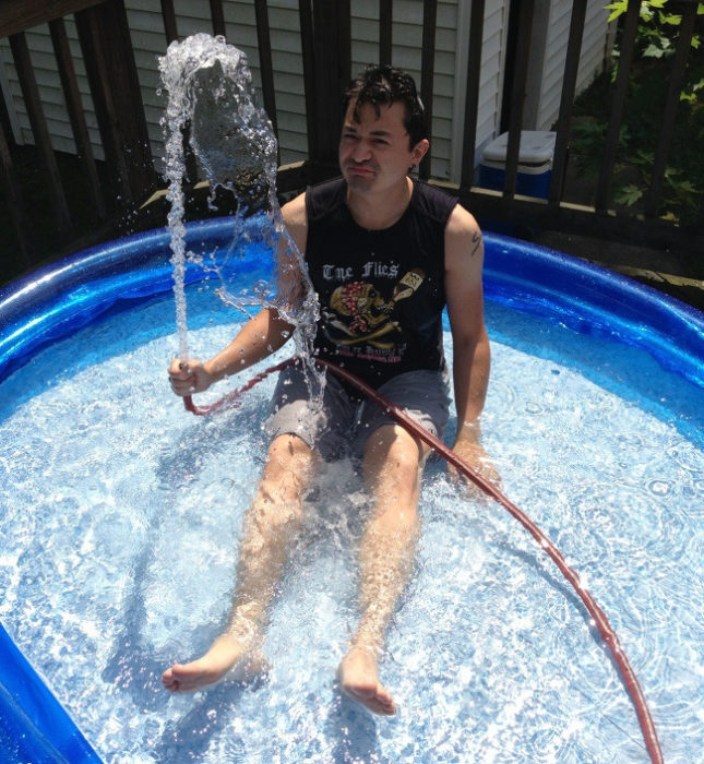 Chico sentado en la piscina jugando con una manguera de agua 