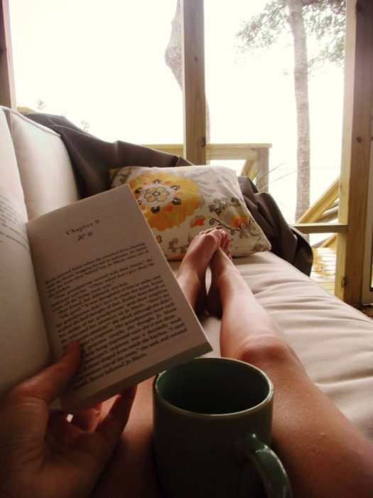 Mujer leyendo, recostada en el sofá, tomando té