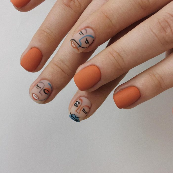 Manicura en tono naranja, con nail art de rostros y efecto mate