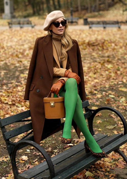 Outfits con medias de colores; mujer sentada en banca de parque, con boina francesa, lentes de sol, saco café, medias verdes, zapatos de animal print