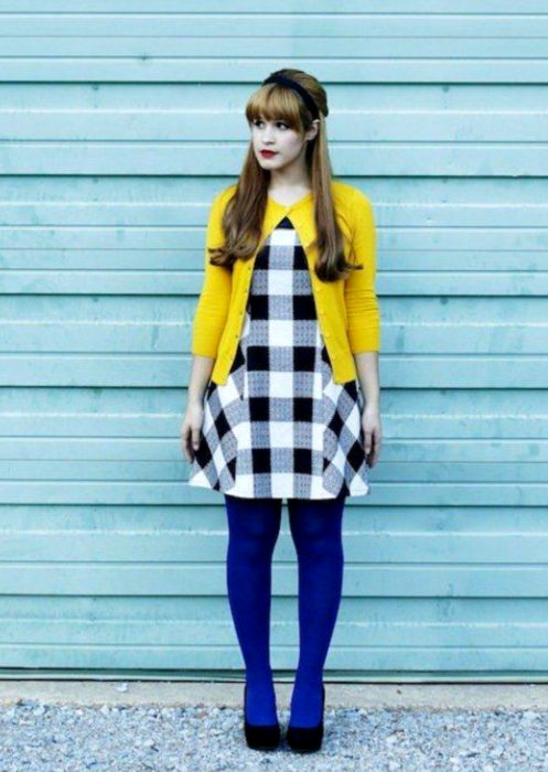 Outfits con medias de colores; chica con vestido blanco con cuadros negros, suéter amarillo y medias azul rey