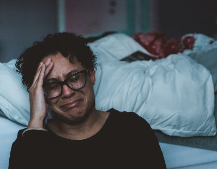 Mujer de lentes y cabello croto llorando en su habitación