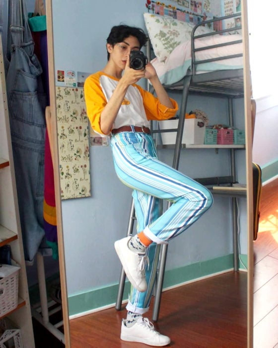 celestialyouth, joven recrea atuendos vintage de Sailor Moon; jeans rayados, tenis blancos, playera blanca con mangas anaranjadas, chico tomándose selfie frente al espejo