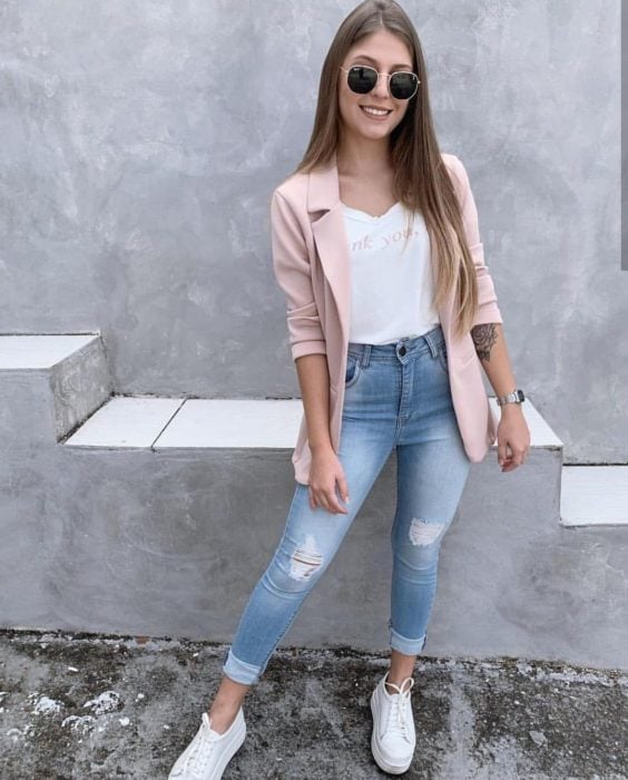 Chica con un outfit de jeans, blazer y blusa rosa con tenis de color blanco 