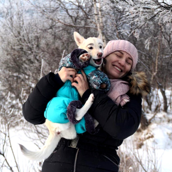 Betty, la perra con cejas; mujer cargando a cachorra blanca y de orejas paradas con suéter en la nieve