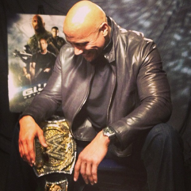 Dwayne Johnson sentado en un sofá mirando su cinturón de la WWE