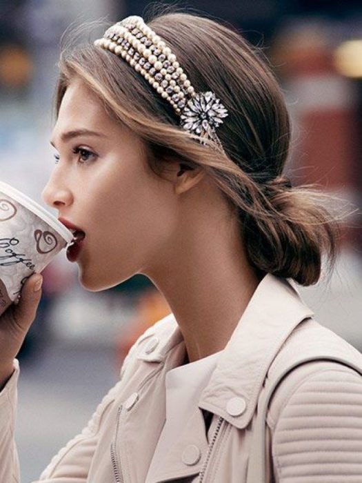 Chica con chaqueta beige tomando café con recogido de cabello adornado con diadema