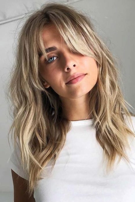 Chica con playera blanca, cabello rubio, mostrando su cabello con corte shag